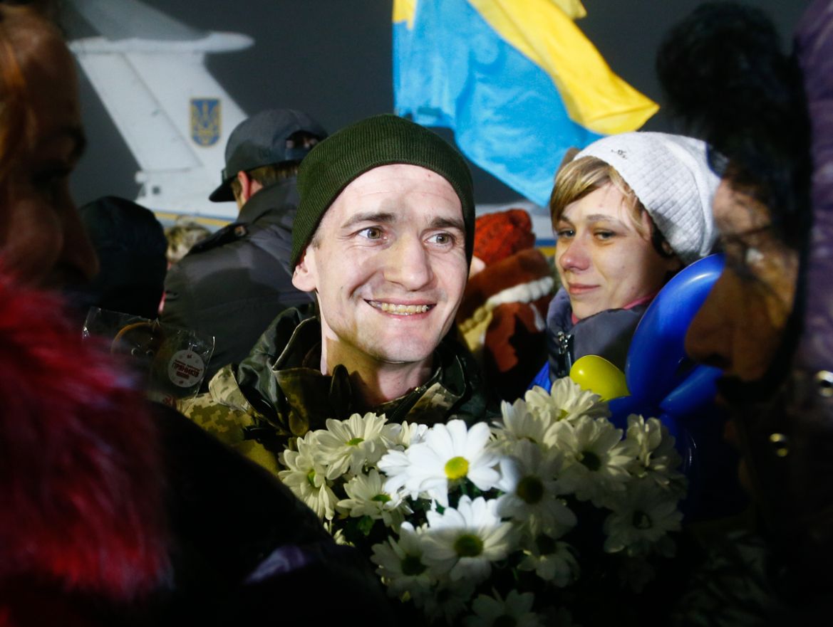 A prisoner who was released by separatists, center, holds flowers smiling as relatives surround him in Kiev Boryspil Airport, Ukraine, early Thursday, Dec. 28, 2017. Ukrainian authorities and Russian-