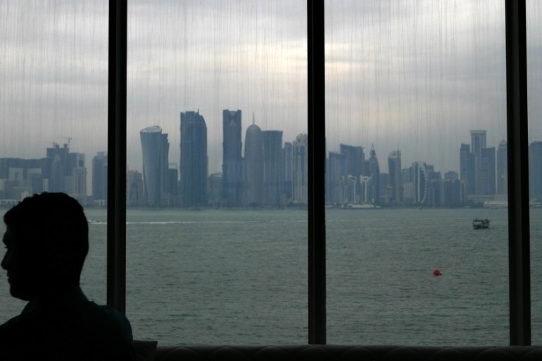 A man sits inside the Islamic art museum of Doha as the city''s skyline is seen in the background in Doha