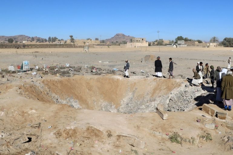 People gather next to a crater caused by an air strike on a graveyard allocated for Houthi fighters in the northwestern city of Saada