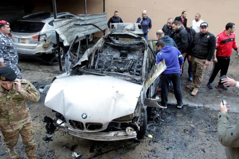 People inspect a damaged car in Sidon