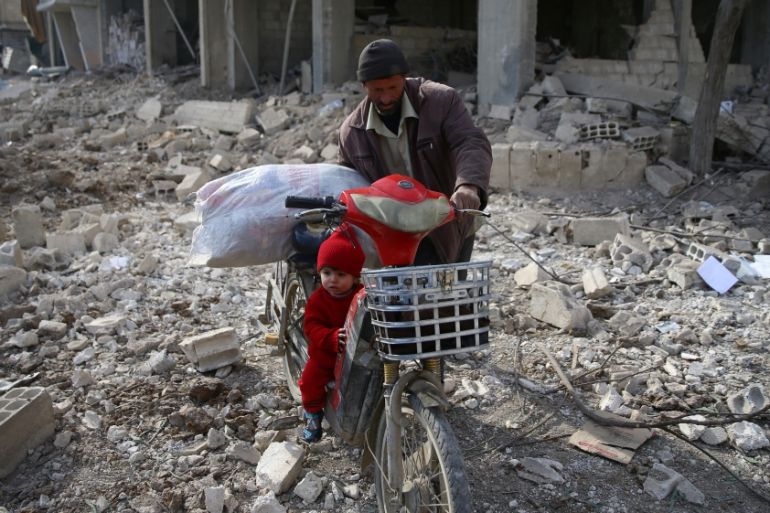 A man is seen with a child who rides a bicycle inside damaged area in Misraba, Eastern Ghouta, near Damascus