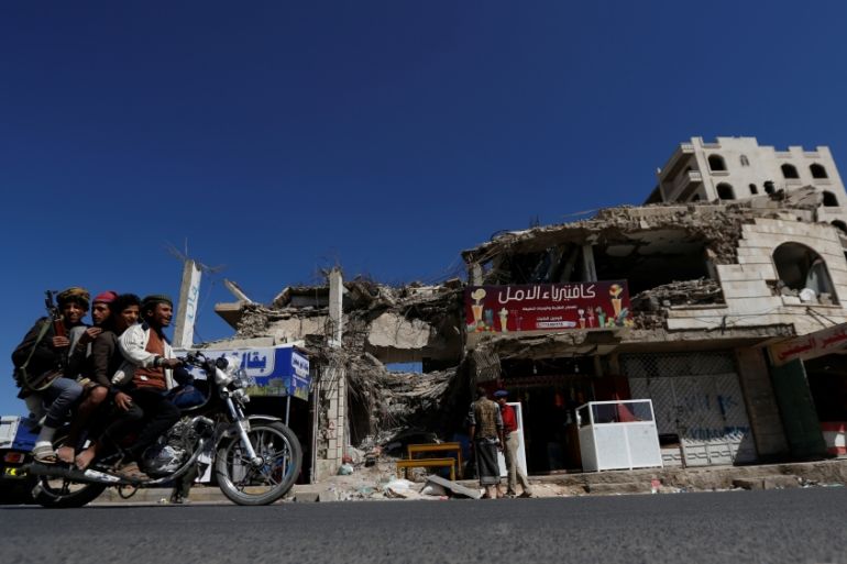 People ride a motorbike past a building hit by air strikes two years ago in Sanaa
