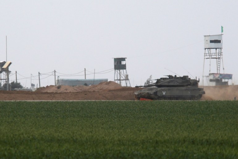 An Israeli tank manoeuvres along the border fence with the southern Gaza Strip, as watch-towers are seen on the Palestinian side near Kibbutz Nirim