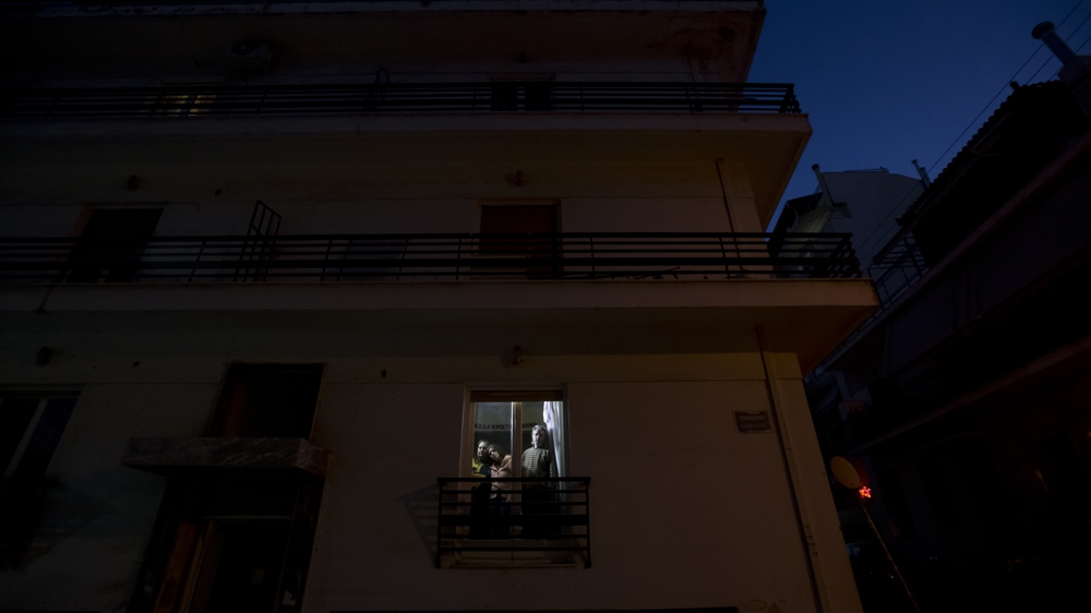 The Filios family stands at the window of their flat in Piraeus [Yannis Kolesidis/Al Jazeera]