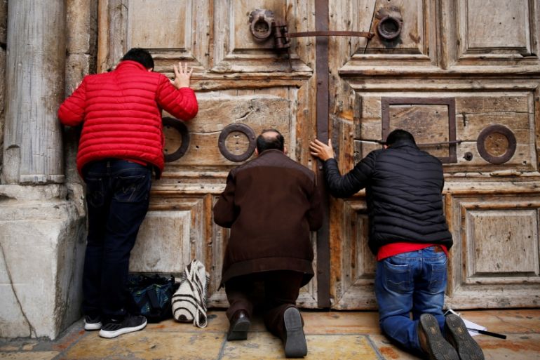Worshippers kneel and pray in front of the closed doors of the Church of the Holy Sepulchre in Jerusalem''s Old City
