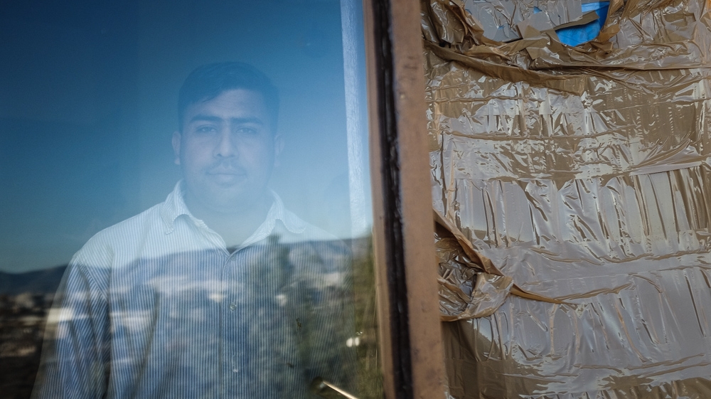 Muhammad Nawaz stands behind a window broken by stones tossed by far-right assailants [Nick Paleologos/SOOC/Al Jazeera]