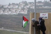 A protester holds the Palestinian flag with the Jewish settlement of Halamish seen in the background [Mohamad Torokman/Reuters]