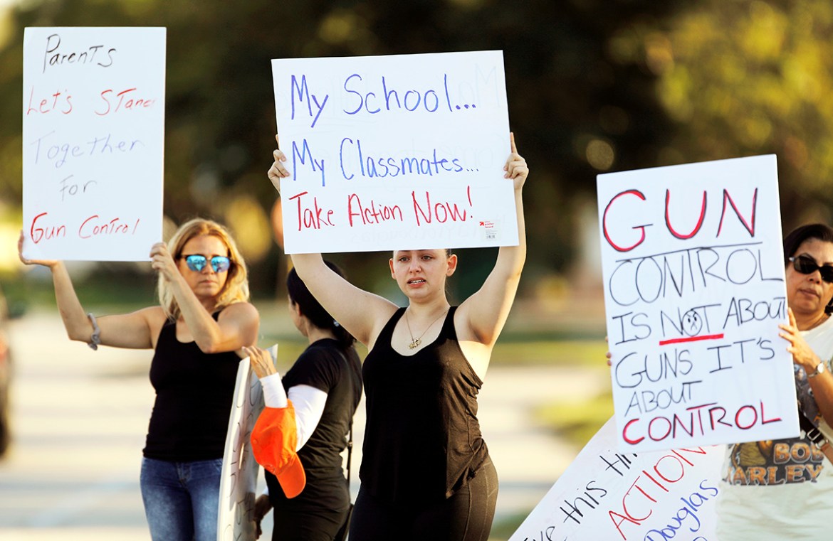 Angelina Lazo (C), an 18-year-old senior at Marjory Stoneman Douglas High School, who said she lost two friends in the shooting at her school two days ago, reacts to honks of support from passing moto