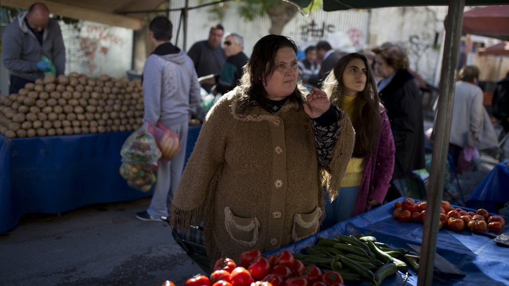 Ioanna seeks vegetables and fruits from a vendor at an outdoor market [Yannis Kolesidis/Al Jazeera]
