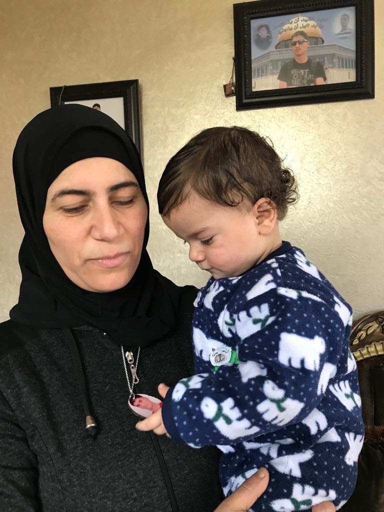 Zeinat Ghneimat holds Abdulla, who plays with a necklace with a picture of his older brother [Rania Zabaneh/Al Jazeera]