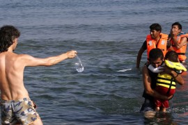 A tourist offers water to migrants as they arrive by paddling an engineless dinghy from the Turkish coast at a beach on the Greek island of Kos [Yannis Behrakis/Reuters]