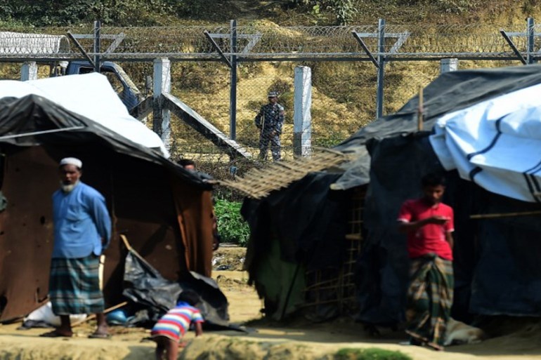 A Myanmar security personnel keeps watch along the Myanmar-Bangladesh border as Rohingya refugee stand outside their makeshifts shelters near Tombru, in the Bangladeshi district of Bandarban