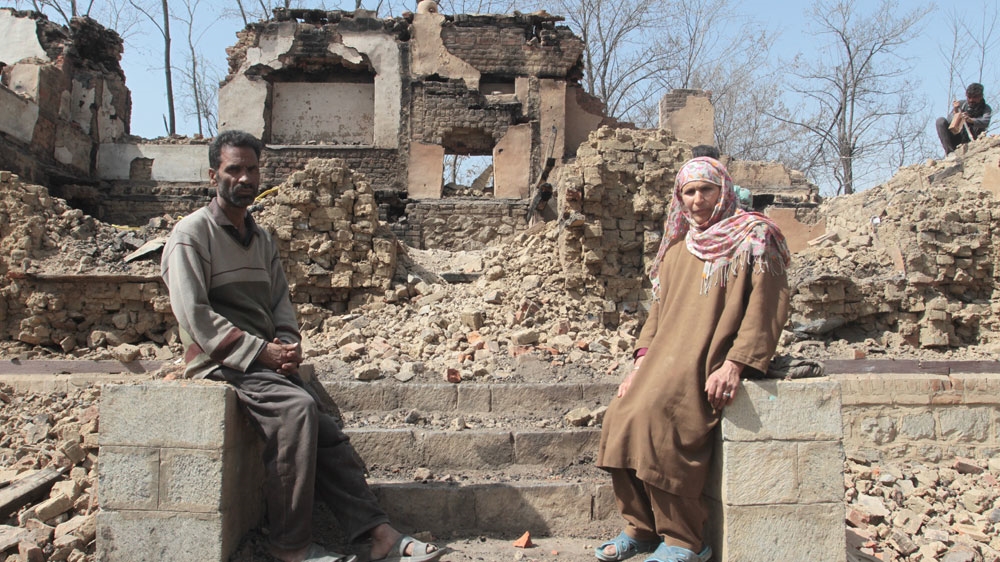 Bhatt and his wife pictured in front of the ruins of their home [Shuaib Bashir/Al Jazeera]
