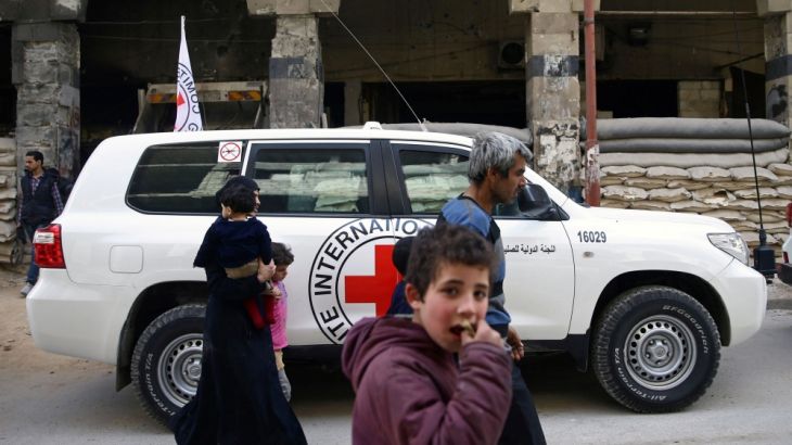 People walk past an International Committee of the Red Cross vehicle in the besieged town of Douma, Eastern Ghouta, in Damascus