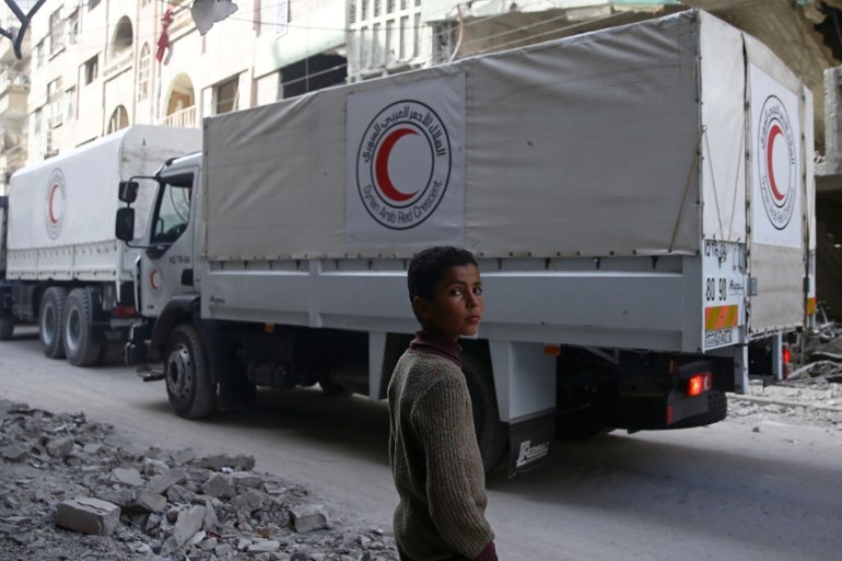 A boy stands as an aid convoy of Syrian Arab Red Crescent drives through the besieged town of Douma