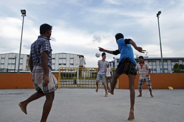 A man plays soccer with migrant workers from Bangladesh and India at a street soccer court near a workers'' dormitory (behind) in Singapore June 3, 2014. REUTERS/Edgar Su