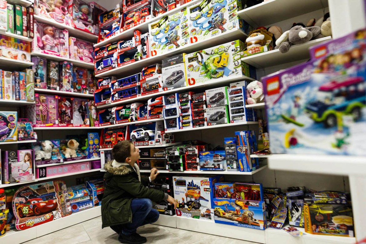 A young boy in a toy shop in Ulcjini. The shelves of toys for boys take up most of the store, with only a small area dedicated to games for girls.