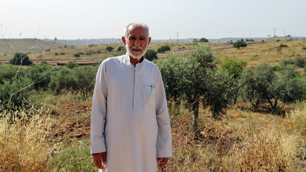 Ahmad al-Shuqair stands in front of Israel's separation fence, which consumed more than 1,000 of his olive trees [Jaclynn Ashly/Al Jazeera]