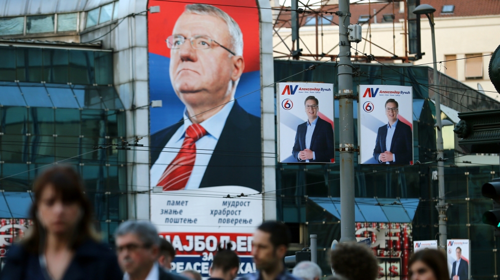 People walk past posters of Seselj and Serbian President Aleksandar Vucic in 2017 [File: Reuters]