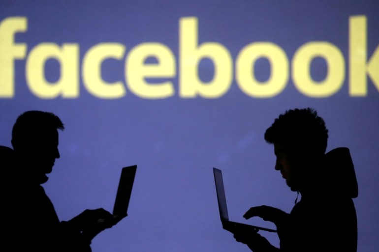 Silhouettes of laptop users are seen next to a screen projection of Facebook logo in this picture illustration