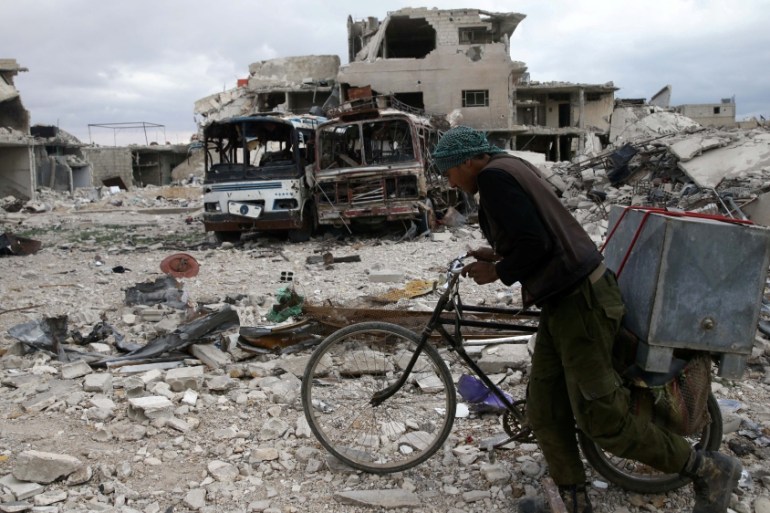 A man walks with his bicycle at a damaged site in the besieged town of Douma