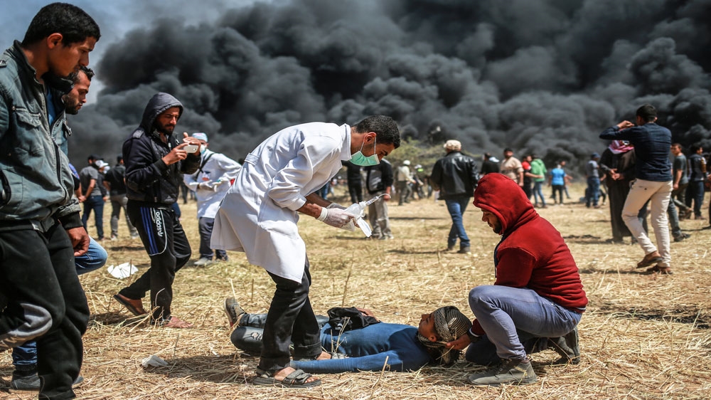 A medic stands over a wounded protester near Gaza Strip's eastern border [Hosam Salem/Al Jazeera]
