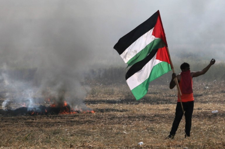 Protester holding Palestinian flags gestures during clashes with Israeli troops at Israel-Gaza border, in the southern Gaza Strip