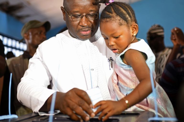 Julius Maada Bio, the presidential candidate for the Sierra Leone People''s Party (SLPP), carries his daughter as he casts his vote during a presidential run-off in Freetown