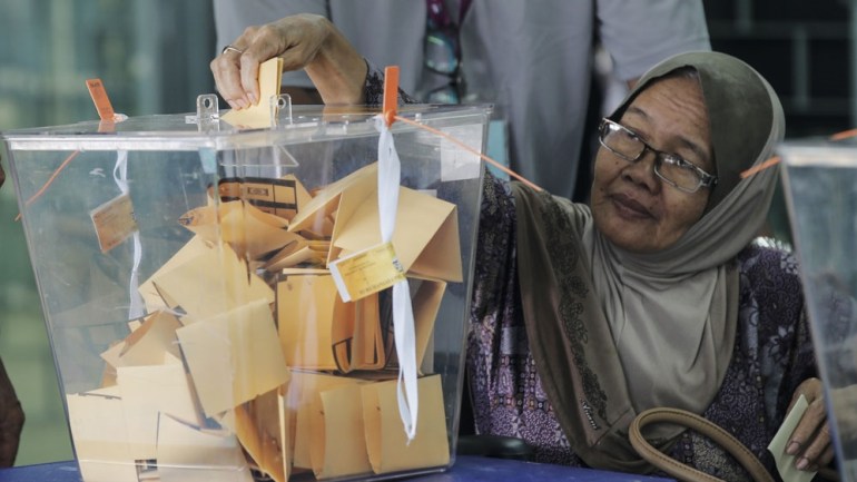 Women puts her yellow ballot paper into a see-through tub which contains other folded papers 