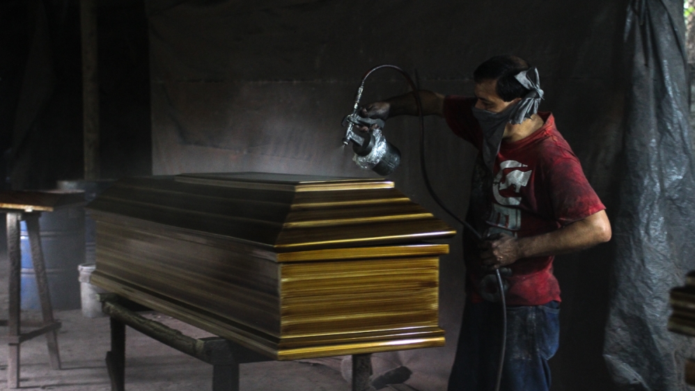 A worker applies sealant to a coffin at a factory in Jucuapa  [Ali Rae/Al Jazeera]