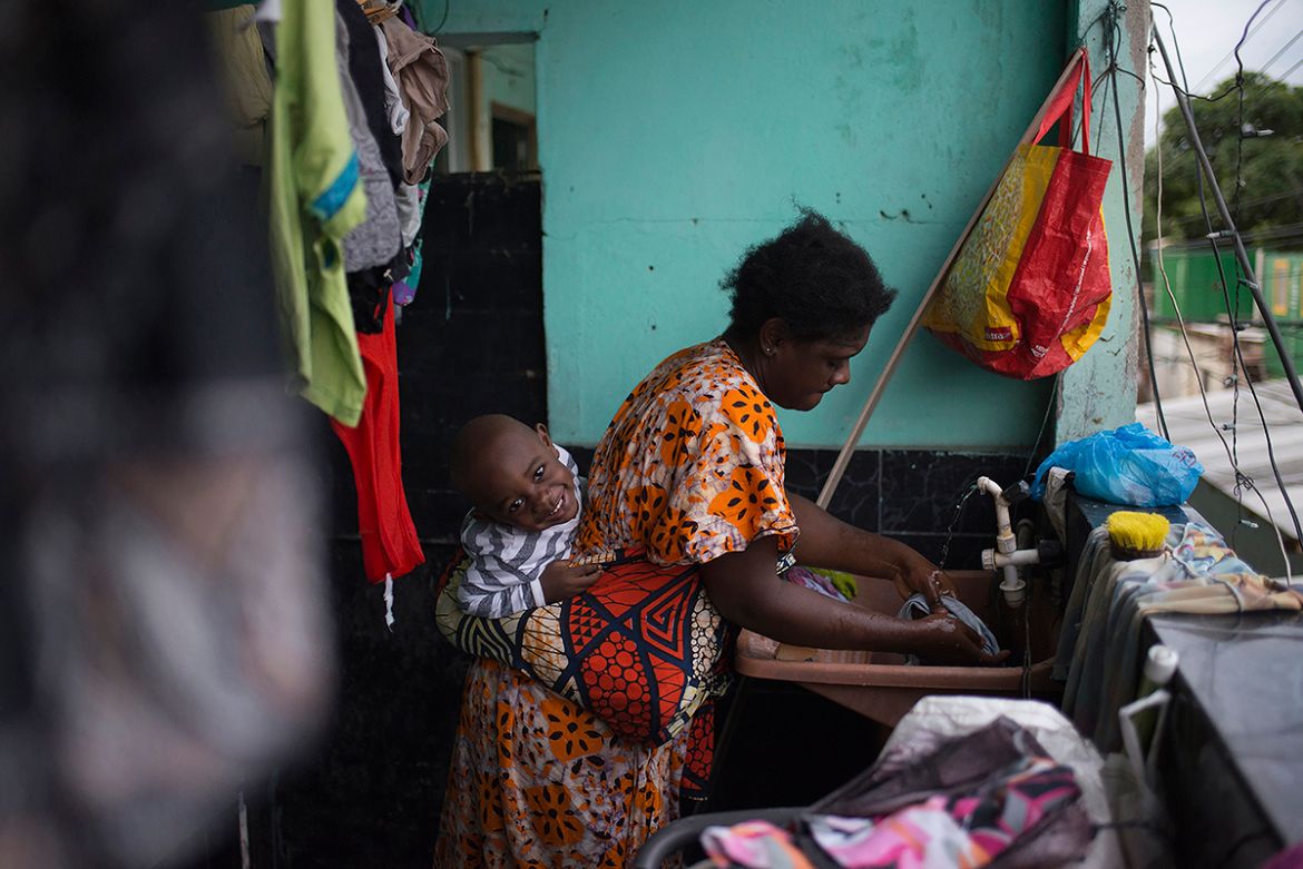 A single mother from the Democratic Republic of Congo, washes clothes with her son in the Bras de Pina favela where she lives in northern Rio. She works at a beauty parlor, styling the hair of African