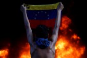 A protester holds a national flag while standing in front of a fire burning during a rally against Venezuela's President Nicolas Maduro, in Caracas [Carlos Garcia Rawlins/Reuters]