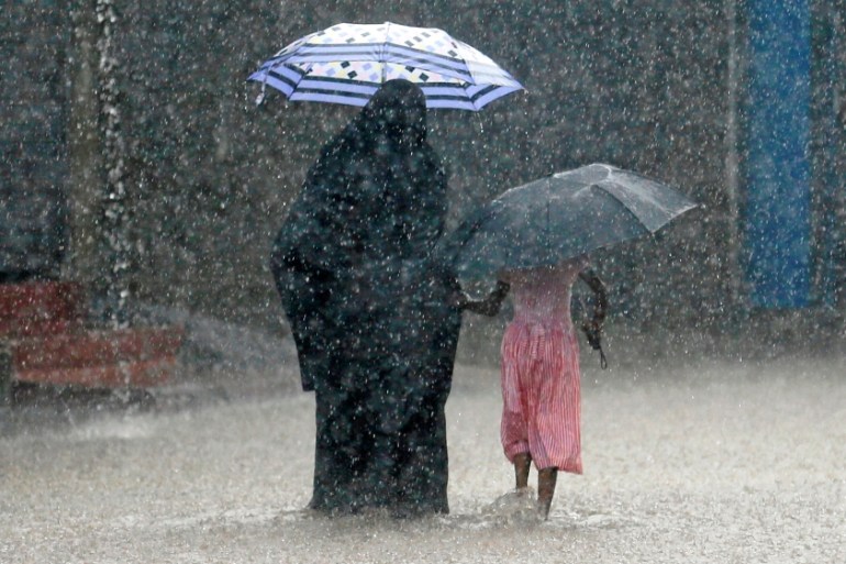 A Muslim woman walks with a girl along a flooded road in the heavy rains in Malawana