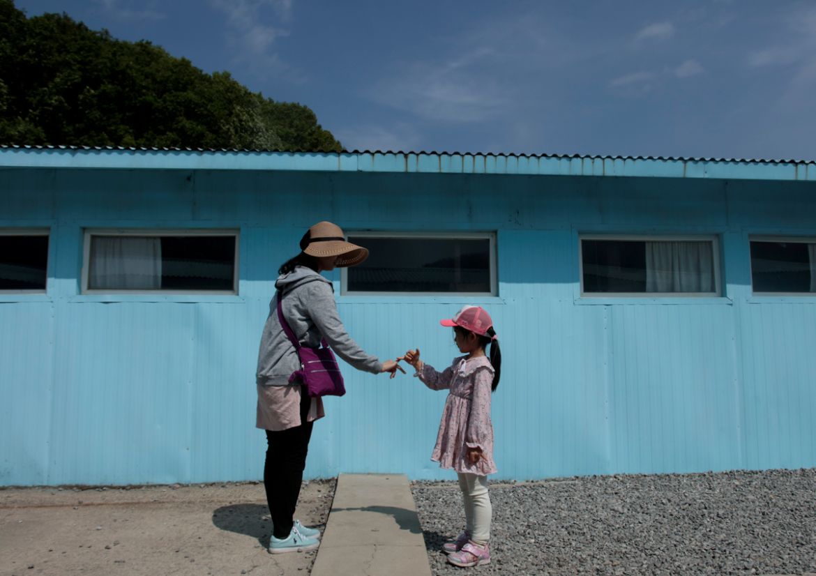 A girl and woman gesture to make a promise over a cement block symbolising a border line as they mimic a handshake between North Korean leader Kim Jong Un and South Korean President Moon Jae-in at the