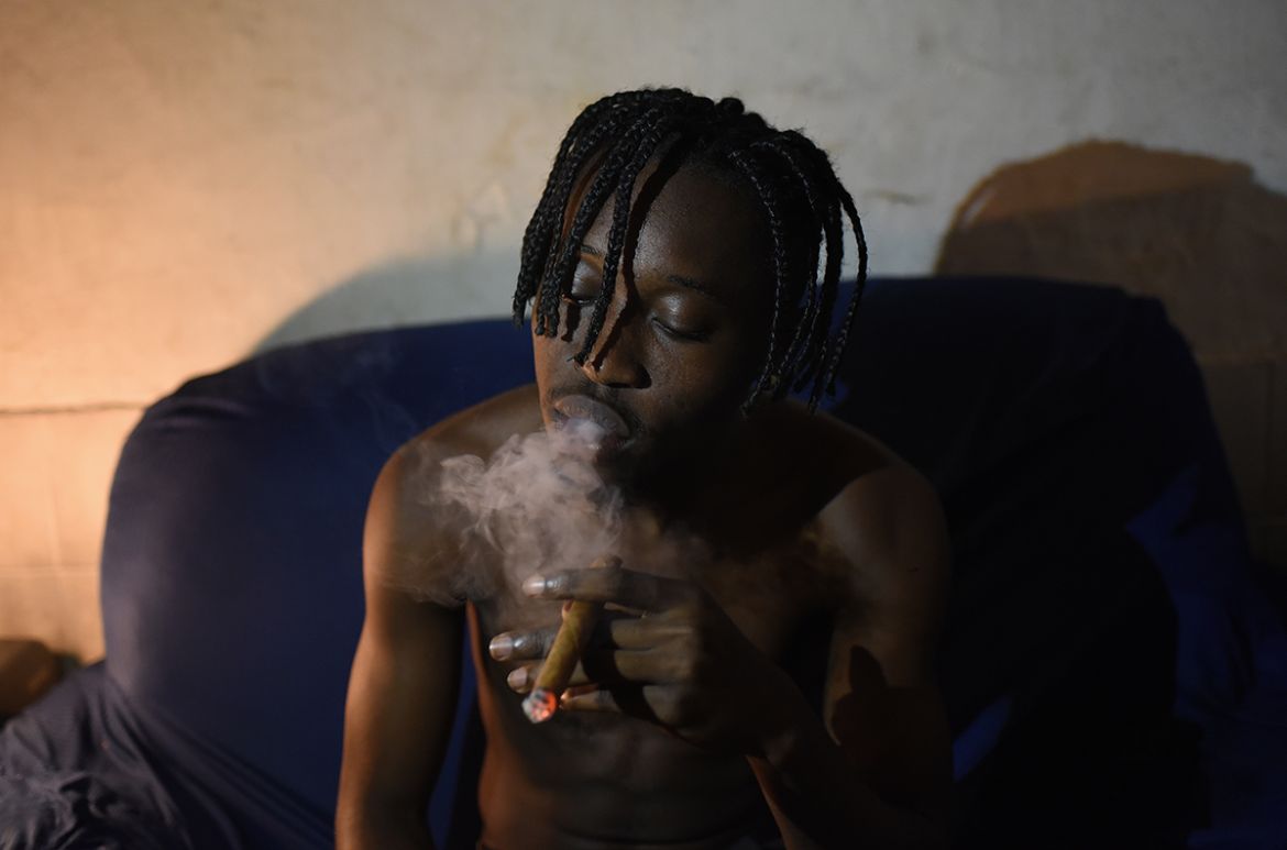 Ali Kembilu Mbemba, 24, a refugee from the Democratic Republic of Congo, smokes a cigar in his home in the Cinco Bocas favela in the north of Rio de Janeiro. With little money, many of the Congolese w