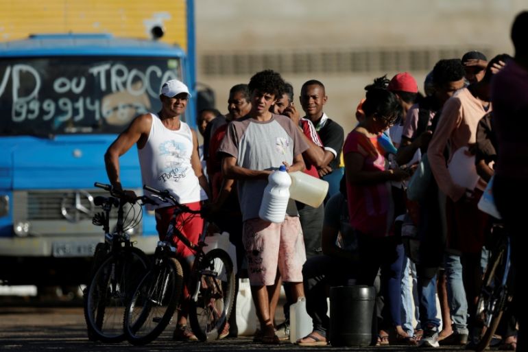 People wait in line to fill their canisters with fuel at a gas station in the outskirts of Brasilia