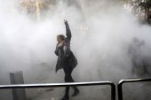 A university student attends a protest inside Tehran University while a smoke grenade is thrown by anti-riot Iranian police on December 30, 2017 [AP]