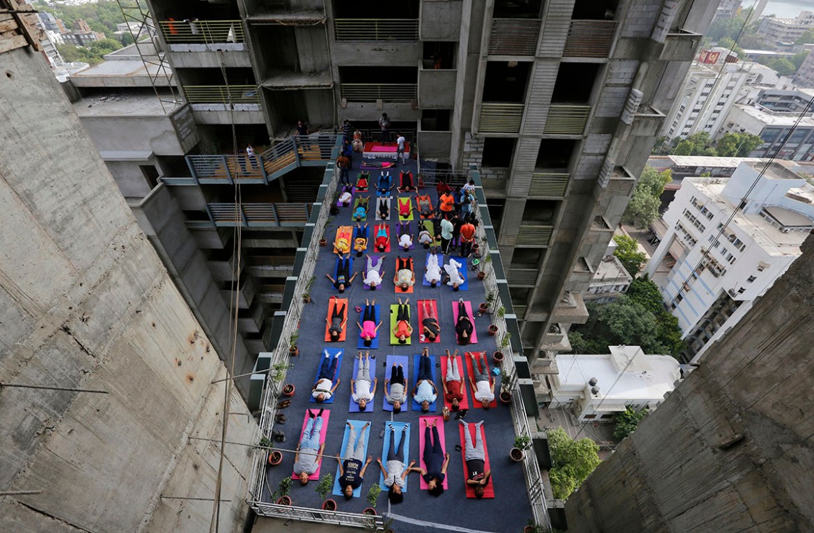 Indians performs yoga on a walk-way between two towers of an under construction high rise residential building as they mark International Yoga Day in Ahmadabad, India, Thursday, June 21, 2018. Yoga en