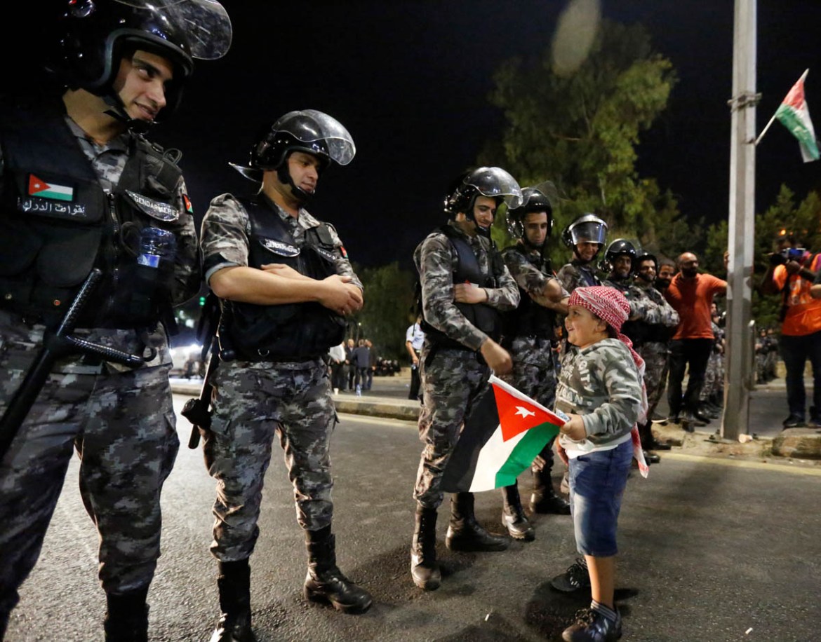 A child who came with his father holds a Jordanian flag while greeting policemen as they stand guard during a protest near Jordan Prime Minister''s office in Amman, Jordan June 5, 2018. REUTERS/Muhamma