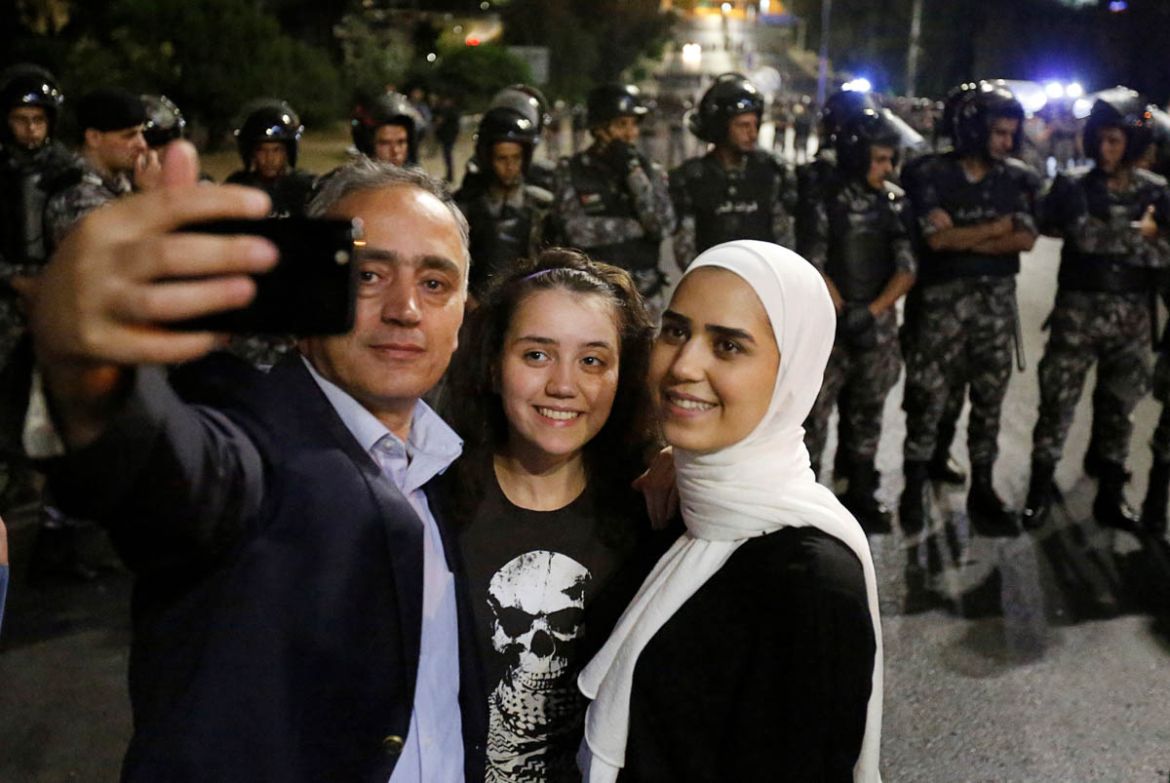 A protester and his daughters take a selfie as policemen stand guard during a protest near Jordan Prime Minister''s office in Amman, Jordan June 5, 2018. REUTERS/Muhammad Hamed