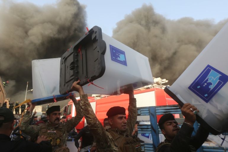Security forces carry ballot boxes as smoke rises from a storage site in Baghdad, housing the boxes from Iraq''s May parliamentary election