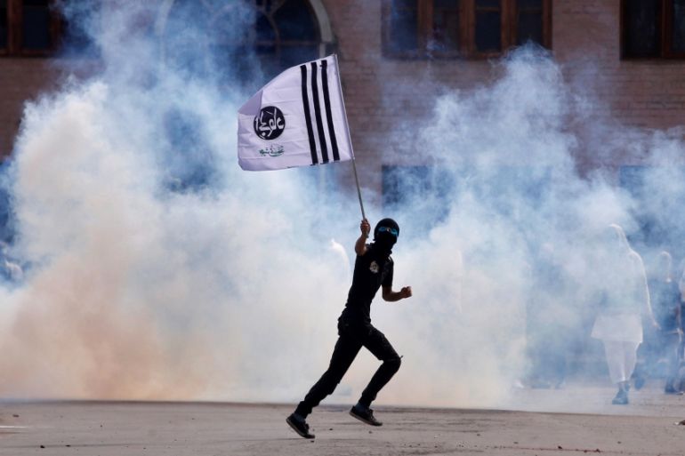 A demonstrator holds a banner as he runs amid smoke from a tear gas shell fired by the Indian police during clashes after the Eid al-Fitr prayers in Srinagar