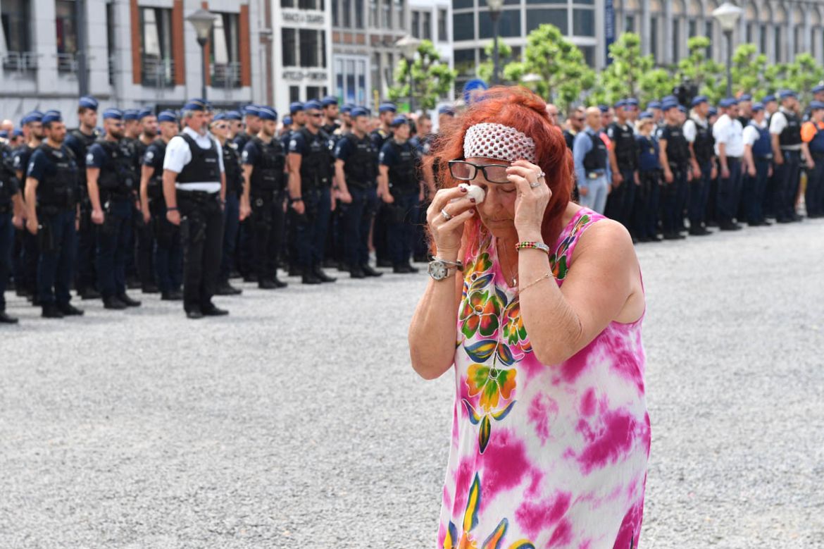 A woman cries as she walks by police officers during a moment of silence for shooting victims near the City Hall in Liege, Belgium, Wednesday, May 30, 2018. A gunman killed three people, including two