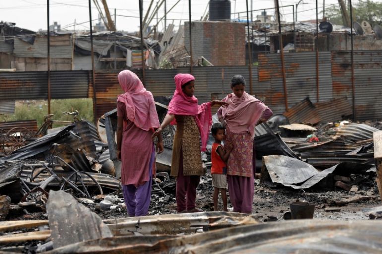 Rohingya women stand on the debris of their houses after a fire broke out in their camp in New Delhi