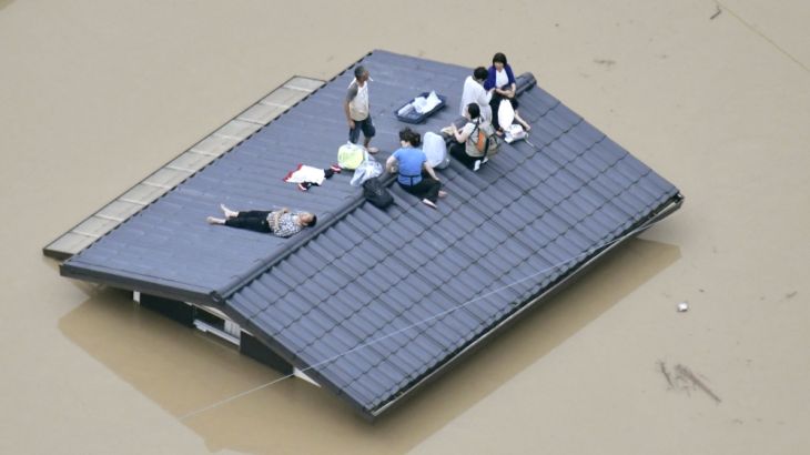 An aerial view shows local residents seen on the roof of submerged house at a flooded area as they wait for a rescue in Kurashiki