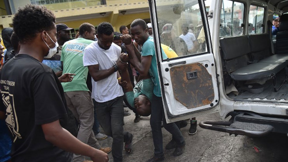 Haitians carry an injured man to an ambulance in the Port-au-Prince commune of Petion-Ville [Hector Retamal/AFP]