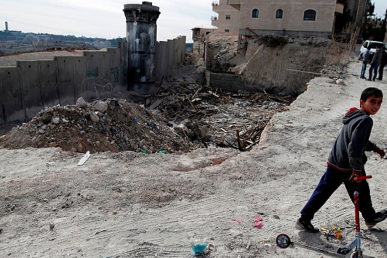 A Palestinian boy walks with his scooter past the rubble of an illegally-built house, which was demolished by Jerusalem municipality workers, in the refugee camp of Shuafat