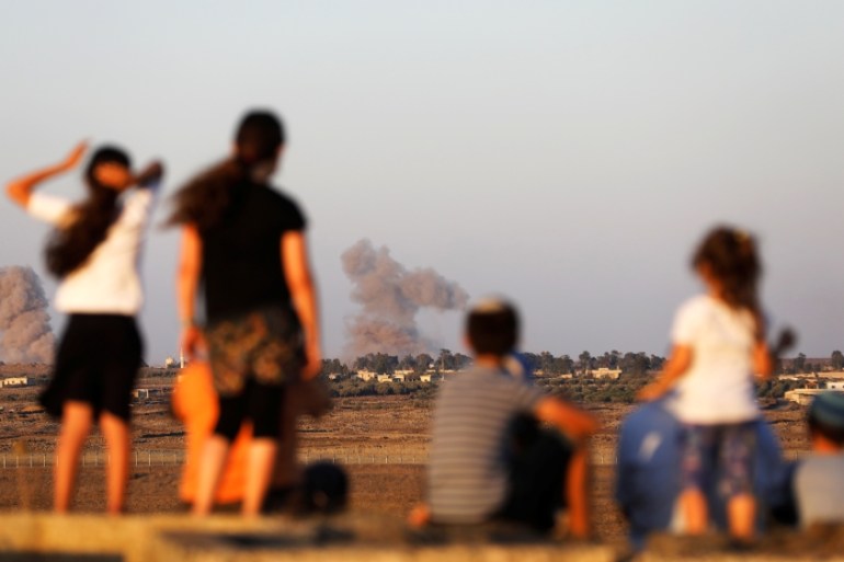 Israeli kids look over the Israeli Syrian border as smoke can be seen following an explosion at its Syrian side it is seen from the Israeli-occupied Golan Heights