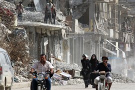Women walk past rubble of damaged buildings in Raqqa