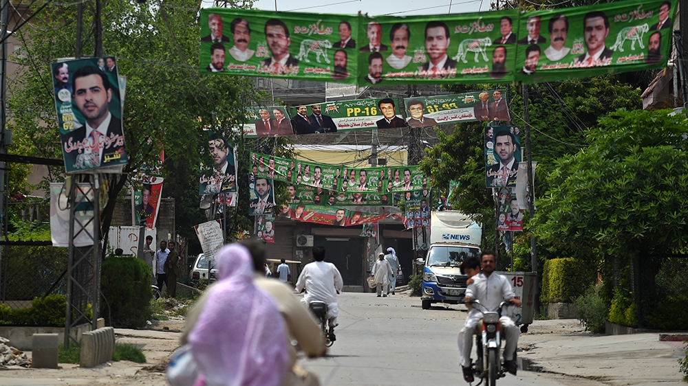 Pakistanis carry on with their day-to-day lives along a road with election banners and posters in Rawalpindi [Wakil Kohsar/AFP]